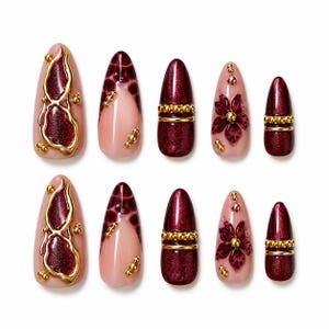 Può includere: Un set di dieci unghie finte con vari design. Le unghie presentano una combinazione di colori bordeaux, oro e nude. Alcune unghie hanno abbellimenti dorati, disegni floreali o finiture glitterate. Le unghie sono di forma ovale.