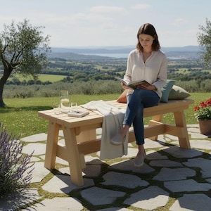 May include: A light-colored wooden bench with a slatted top and sturdy legs, featuring a clear glass pitcher, two small glasses, and a book placed on the surface, alongside a draped white textile, positioned on a stone patio.