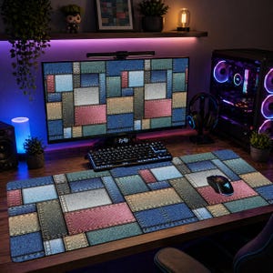 May include: A large rectangular desk mat with a patchwork denim design in shades of blue, pink, and gray. A computer mouse rests on the mat. The computer monitor and keyboard also display the same denim patchwork pattern.