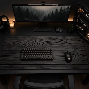 May include: A black computer setup featuring a monitor displaying a forest scene, a keyboard, and a mouse. The desk has a wood grain pattern. A computer tower and headphones are also visible, creating a modern workspace.