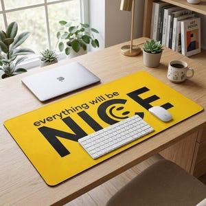 Peut inclure: Un tapis de bureau rectangulaire jaune avec l'inscription "everything will be NICE" en noir et un smiley. Un clavier et une souris blancs sont sur le tapis. Un ordinateur portable et une tasse sont également sur le bureau.