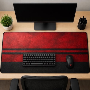 Puede incluir: Una alfombrilla de escritorio rectangular grande en rojo y negro. La parte superior es roja con un aspecto texturizado, separada por dos rayas negras de la sección inferior negra. Un teclado y un ratón negros están sobre la alfombrilla.