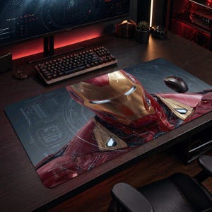 Könnte beinhalten: Rechteckiges Mauspad mit detailliertem Bild von Iron Mans Helm und Brust. Das Design beinhaltet Rot-, Gold- und Silbertöne mit einem schematischen Hintergrund. Eine schwarze Maus und Tastatur sind sichtbar.