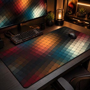 May include: A large rectangular mouse mat featuring a geometric pattern of squares in shades of red, orange, yellow, green, and blue. A black mouse and keyboard are on the desk. The computer monitor displays a matching pattern.