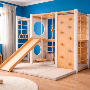 May include: A wooden indoor climbing frame with a slide, climbing wall, and monkey bars. The structure is light-coloured with a white frame and sits on padded mats. A giraffe toy and teddy bears are nearby.
