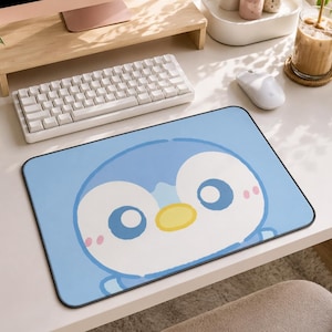 Peut inclure: Un tapis de souris rectangulaire avec un fond bleu clair et un grand motif central représentant un visage de pingouin de dessin animé. Le pingouin a un visage blanc, de grands yeux bleus, un petit bec jaune et des joues roses.