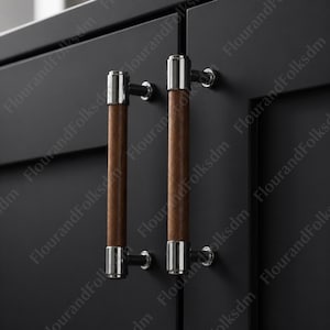 May include: Two cabinet pulls with a modern design. Each pull features a cylindrical, dark brown wooden handle with polished silver-tone metal accents on each end. The pulls are mounted on a black cabinet door.