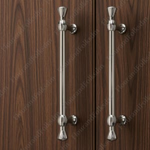 May include: Two brushed nickel cabinet pulls with a decorative design. The pulls are vertically oriented and mounted on a dark wood cabinet door. Each pull has a decorative top and bottom.