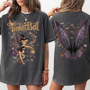 May include: A charcoal gray oversized t-shirt featuring a front graphic of Tinker Bell wearing a witch hat with the text TinkerBell above. The back of the shirt displays large, detailed purple and black fairy wings surrounded by small orange pumpkins and bats.