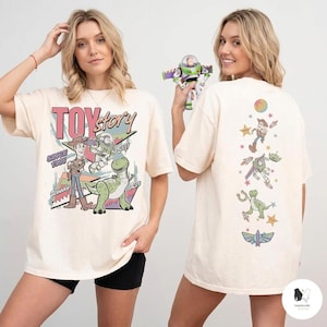 K&ouml;nnte beinhalten: Cremefarbenes T-Shirt mit einem Toy Story-Motiv. Das Design auf der Vorderseite zeigt Woody, Buzz Lightyear, Rex und den Text "TOY STORY SINCE 1995". Die R&uuml;ckseite des Shirts zeigt verschiedene Toy Story-Charaktere und Sterne.