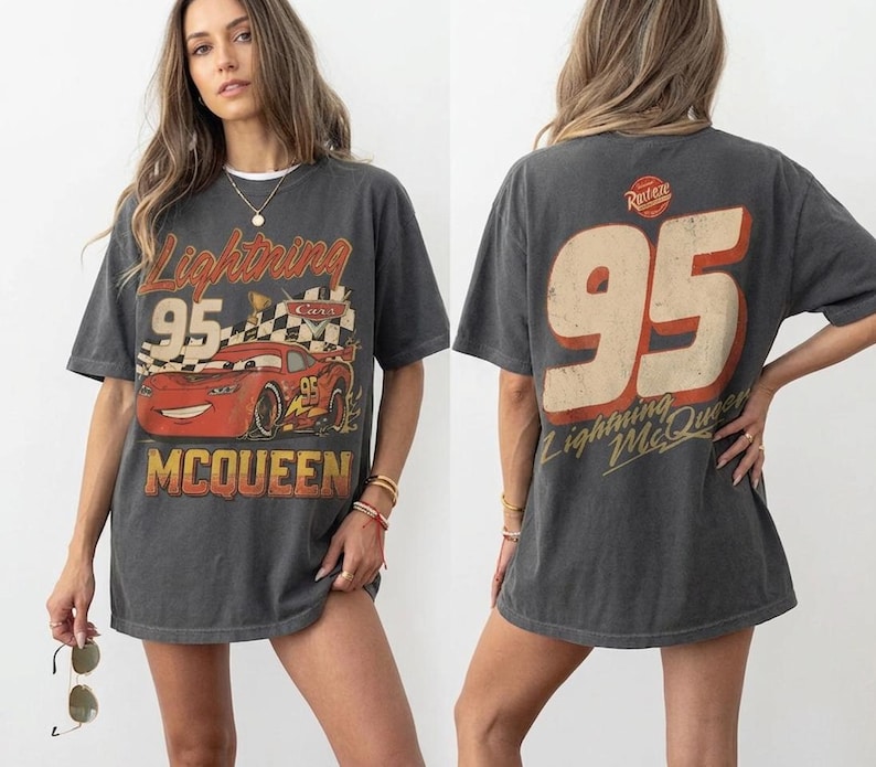 K&ouml;nnte beinhalten: Dunkelgraues T-Shirt mit einer Grafik von Lightning McQueen aus dem Film Cars. Auf der Vorderseite steht "Lightning 95 McQueen" mit einem roten Rennwagen. Auf der R&uuml;ckseite steht gro&szlig; "95" und der Text "Lightning McQueen".