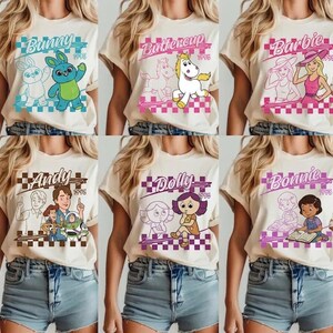 Pode incluir: Seis camisetas creme com diferentes designs de personagens de desenhos animados. Cada camisa apresenta o nome de um personagem e o ano de 1995 em uma caixa quadriculada. Os personagens incluem Bunny, Buttercup, Barbie, Andy, Dolly e Bonnie.