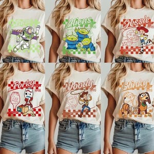 Pode incluir: Seis camisetas bege com personagens de Toy Story: Buzz Lightyear, Aliens, Jessie, Forky, Woody e Slinky. Cada camisa tem um gr&aacute;fico de personagem com o nome do personagem e o ano de 1995.