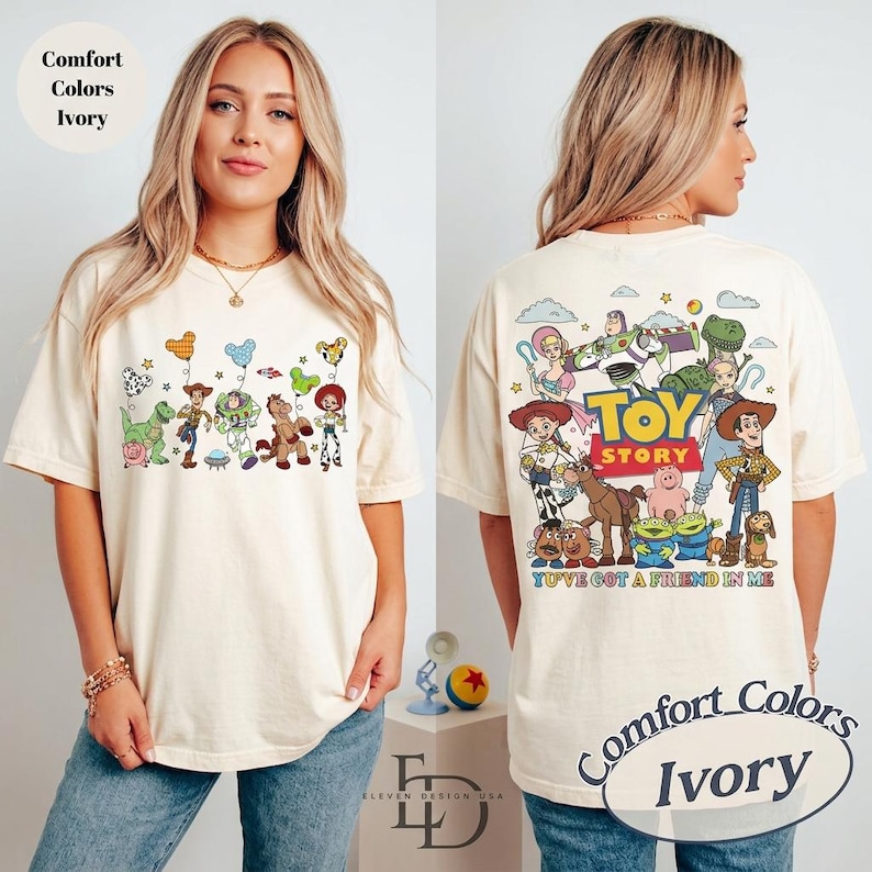 May include: Ivory-colored t-shirt featuring Toy Story characters on the front and back. The front displays characters with balloons, while the back showcases a larger group with the text "Toy Story" and "You've Got a Friend in Me."