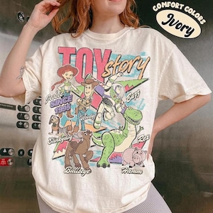 Puede incluir: Camiseta de color marfil con un gr&aacute;fico de personajes de Toy Story, incluyendo a Woody, Buzz y Jessie. El dise&ntilde;o incluye el texto "TOY STORY" y "SINCE 1995". La camiseta tiene mangas cortas y un corte relajado.