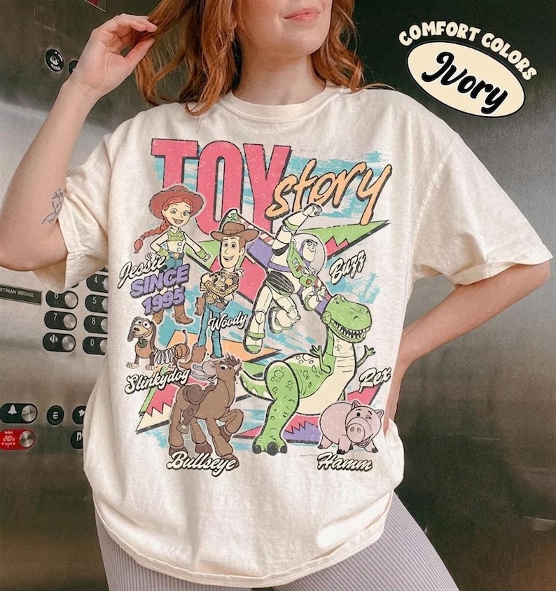 Puede incluir: Camiseta de color marfil con un gr&aacute;fico de personajes de Toy Story, incluyendo a Woody, Buzz y Jessie. El dise&ntilde;o incluye el texto "TOY STORY" y "SINCE 1995". La camiseta tiene mangas cortas y un corte relajado.