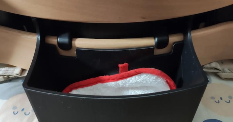 Puede incluir: Un contenedor de almacenamiento negro con un asa de madera y un guante de cocina rojo y blanco en el interior. El contenedor est&aacute; montado debajo de una superficie de madera y el guante tiene un borde rojo.