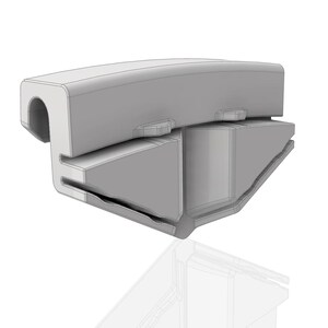 Op de afbeelding: Een lichtgrijs, driedimensionaal object met een gebogen bovenkant en een rechthoekige basis. Het object heeft een uitgehold gedeelte aan &eacute;&eacute;n uiteinde en verschillende uitstekende elementen. Het ontwerp lijkt een onderdeel of deel van een grotere structuur te zijn.