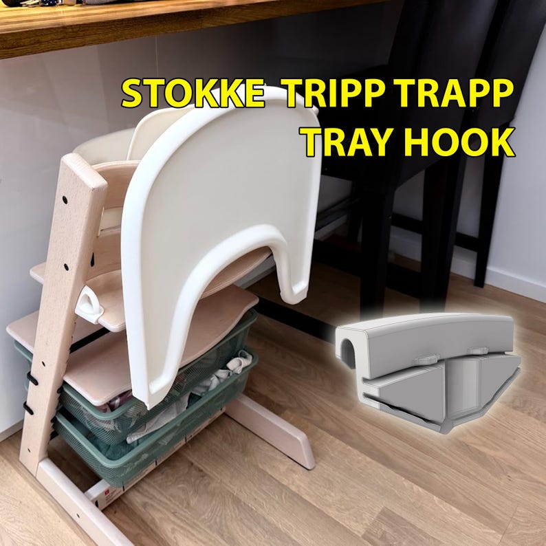 Op de afbeelding: Een Stokke Tripp Trapp kinderstoel met een wit dienblad en een grijze dienbladhaak. De kinderstoel is gemaakt van licht hout en heeft een wit dienblad. De tekst "STOKKE TRIPP TRAPP TRAY HOOK" is geel.