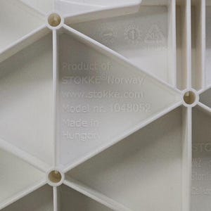 Op de afbeelding: Close-up van een wit kunststof onderdeel met een geometrisch ontwerp. De tekst "Product of STOKKE Norway" en "Model nr. 1048052" zijn zichtbaar. Het onderdeel is gemaakt in Hongarije.