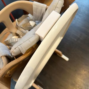 Op de afbeelding: Een lichtgekleurde houten kinderstoel met een wit dienblad en een grijs patroon kussen. De stoel heeft een veiligheidsharnas en een voetensteun. De lade is ongeveer 46 cm breed.