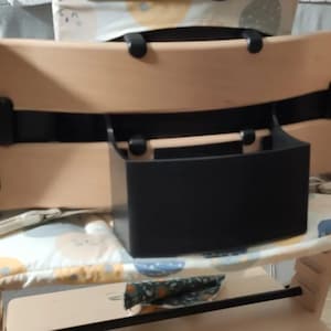 Puede incluir: Una trona de madera clara con una caja de almacenamiento negra. La silla tiene un coj&iacute;n estampado y est&aacute; dise&ntilde;ada para beb&eacute;s y ni&ntilde;os peque&ntilde;os. La silla es de madera.