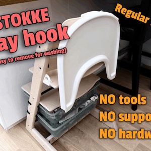 Op de afbeelding: Een beige Stokke dienbladhaak met de tekst "STOKKE tray hook (gemakkelijk te verwijderen om te wassen)". De afbeelding bevat ook de tekst "Regular PLA!", "NO tools", "NO supports" en "NO hardware". De haak is bevestigd aan een houten kinderstoel.