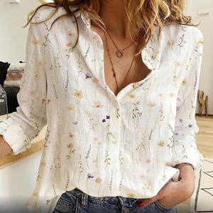 Può includere: Camicia bianca con bottoni con un delicato motivo floreale nei toni del giallo, viola e pesca. La camicia a maniche lunghe ha un colletto classico ed è realizzata in un tessuto leggero, perfetta per un look casual e femminile.