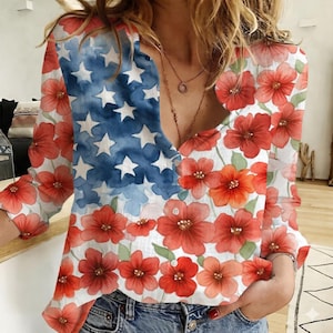 May include: A button-down shirt with a patriotic design. The left side features a watercolor American flag with white stars on a blue background. The right side and sleeves are covered in red and orange floral patterns on a white background.