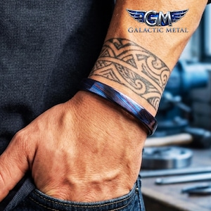 Puede incluir: Un brazalete de metal azul y morado. El brazalete se lleva en una muñeca con un tatuaje tribal. El logotipo de Galactic Metal es visible en la esquina superior derecha.