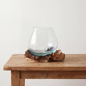Könnte beinhalten: Eine klare Glasschale mit wellenförmigem Design am Boden, die auf einem Stück Naturholz ruht. Das Holz hat eine raue, strukturierte Oberfläche und eine warme braune Farbe. Die Schale ist leer und steht auf einem Holztisch.