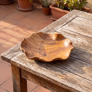 Könnte beinhalten: Eine handgefertigte Holzschale mit einer einzigartigen, organischen Form. Die Schale besteht aus hellbraunem Holz mit sichtbaren Maserungsmustern. Sie steht auf einem verwitterten Holztisch und zeigt ihre natürliche Schönheit und Handwerkskunst.