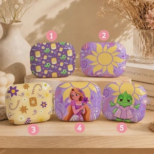 May include: Five rectangular protective cases for wireless earbuds, each featuring distinct designs with purple, yellow, and white color palettes. The cases display patterns of lanterns, suns, flowers, a cartoon character with long hair, and a green lizard.