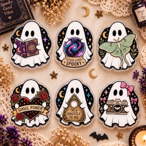 May include: Six die-cut stickers featuring white ghosts. One holds a purple book, one a galaxy crystal ball with text 'FUTURE LOOKS SPOOKY', one a green moth, one a heart with 'GHOUL POWER', one a planchette with 'TALK GHOSTLY TO ME', and one a camera with 'SPOOKY SNAPS'.