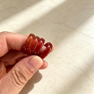 May include: A set of four smooth, translucent, deep reddish-brown rings stacked together. The rings have a rounded, polished surface and a consistent circular shape, displaying a rich, warm color tone that catches the light across their curved edges.