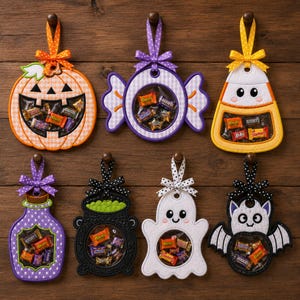 Könnte beinhalten: Sechs hängende Halloween-Leckerli-Halter aus Filz mit durchsichtigen Kunststofffenstern, gefüllt mit verschiedenen Süßigkeiten. Die Motive umfassen einen Kürbis, ein Bonbon, einen Zuckermais, eine Flasche, einen Kessel, ein Gespenst und eine Fledermaus.