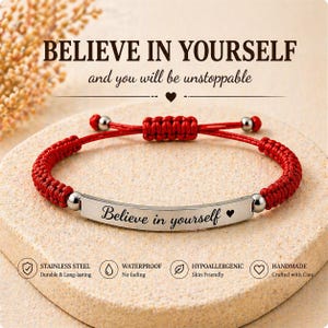 May include: A red braided bracelet with a silver bar engraved with "Believe in yourself" and a heart symbol. The bracelet has adjustable sliding knots and is displayed on a textured surface. The text "BELIEVE IN YOURSELF" is at the top.