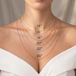 Puede incluir: Una selecci&oacute;n de delicados collares de cadena en tonos oro, plata y oro rosa, exhibidos sobre una persona. Los collares var&iacute;an en longitud, con etiquetas que indican tama&ntilde;os de 35,5 cm a 61 cm.