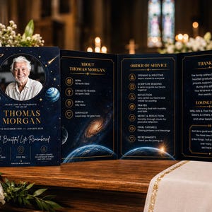 May include: A tri-fold funeral program featuring a dark blue space theme with planets and stars. The front displays a portrait of Thomas Morgan, his name, and dates. The interior panels include sections for About Thomas Morgan, Order of Service, and Thank You.