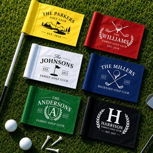 May include: Six rectangular golf flags in yellow, red, white, blue, green, and black, each featuring custom family names, established dates, and golf-themed graphics. A white flagstick, two white golf balls, and three white tees are included.