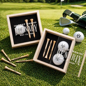 Könnte beinhalten: Zwei Golfball- und Tee-Sets in Holzrahmen auf grünem Gras. Jedes Set enthält Golfbälle, Holztees und den Text "Best Man" und Namen. Ein Set hat den Text "Barnaby May 13, 2026". Das andere Set hat den Text "Hendrix May 13, 2026".