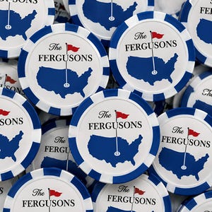May include: A collection of round white poker chips with blue striped edges. Each chip features a blue silhouette of the United States map, a black golf flag pole with a red flag, and the black text The FERGUSONS printed on the surface.