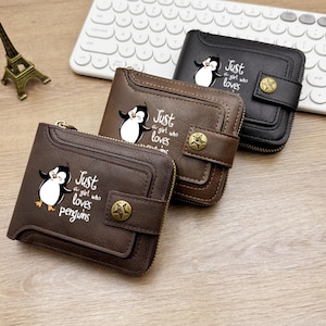 Puede incluir: Tres carteras plegables en negro y marrón con un gráfico de pingüino y el texto Just a girl who loves penguins. Cada cartera incluye un cierre de botón a presión con un emblema de estrella y una cremallera lateral para almacenamiento seguro.