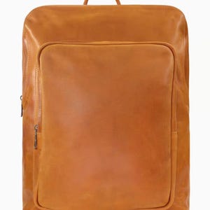 Peut inclure: Sac à dos rectangulaire en cuir de couleur tan, avec une poche avant et une poignée supérieure. Il possède une fermeture éclair latérale et une plus petite sur la poche avant. Le cuir a un aspect lisse et légèrement texturé.