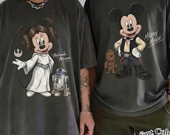 May include: Two charcoal gray t-shirts featuring Star Wars themed graphics. The left shirt displays Minnie Mouse as Princess Leia with R2-D2 and the text Minnie Mouse. The right shirt shows Mickey Mouse as Han Solo with Chewbacca and the text Mickey Mouse.