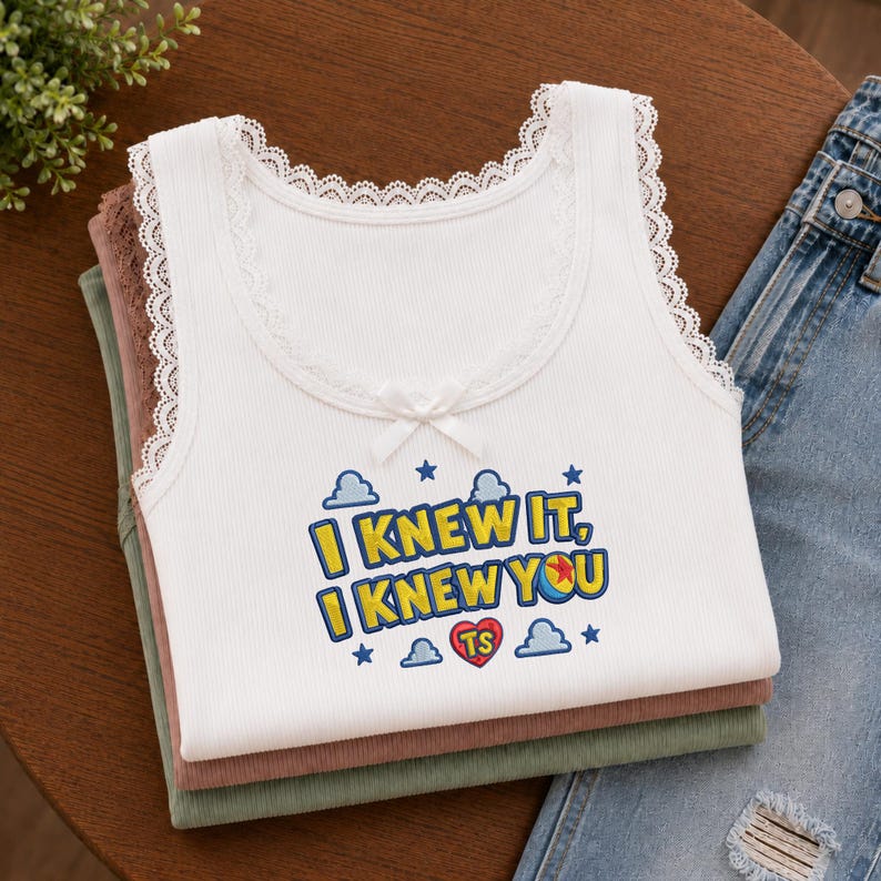 May include: A white ribbed tank top with lace trim along the neckline and armholes, featuring a small white bow at the center. The graphic print reads I KNEW IT, I KNEW YOU with blue clouds, stars, and a red heart containing the letters TS.