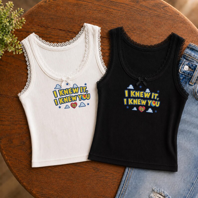 May include: Two ribbed tank tops, one white and one black, featuring lace trim along the neckline and armholes, a small center bow, and a graphic print that reads I KNEW IT, I KNEW YOU with clouds, stars, and a heart containing the letters TS.