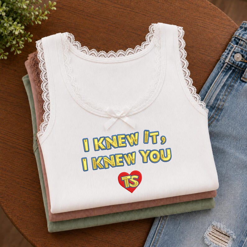 Puede incluir: Una camiseta de tirantes blanca acanalada con ribete de encaje en el cuello y las sisas, con un peque&ntilde;o lazo blanco en el centro. El texto I KNEW IT, I KNEW YOU est&aacute; impreso en amarillo con bordes azules sobre un coraz&oacute;n rojo con TS.