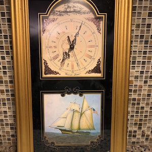 May include: A rectangular wall clock with a gold frame. The upper section features a clock face with Roman numerals and the text "Russell's London". The lower section displays a painting of a sailing ship with an American flag on the water.