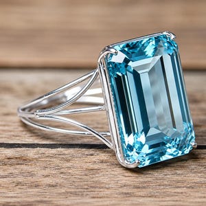 May include: A silver-toned ring featuring a large, rectangular, emerald-cut light blue gemstone held by four prongs. The band consists of three thin, parallel silver-toned wires that converge into a single shank at the back of the ring.